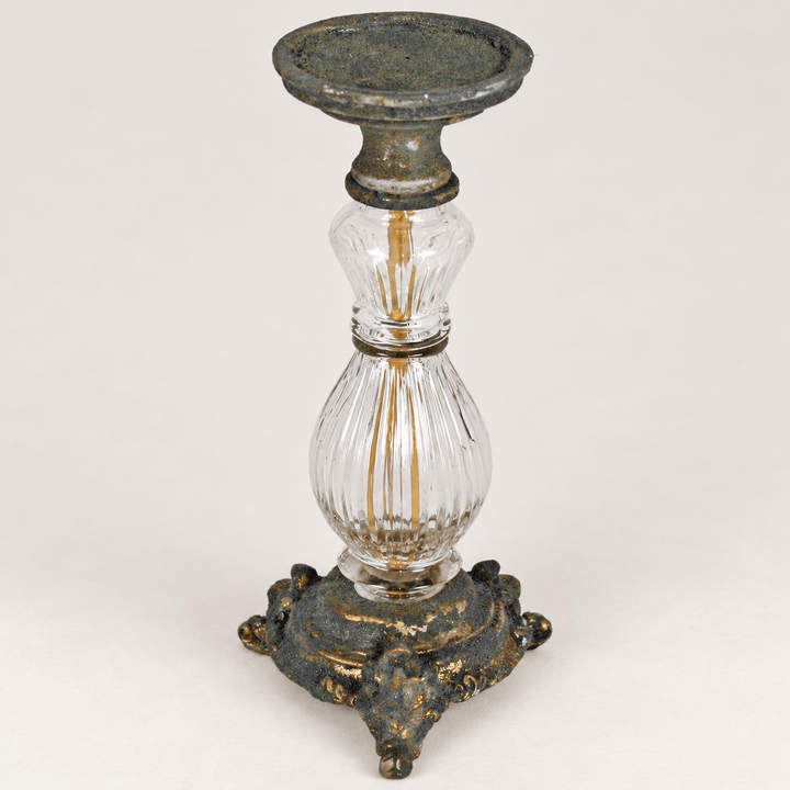 Antiikkityylinen kynttilänjalka, jossa on kirkas uurrettu lasivarsi sekä patinoidun näköinen metallijalusta ja kynttiläalusta. / Antique-style candle holder with a clear fluted glass stem, distressed metal base and candle plate.