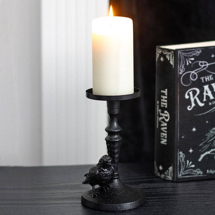 Musta Mystic Raven -kynttilänjalka valkoisen pöytäkynttilän kanssa, korppi pyöreällä jalustalla.