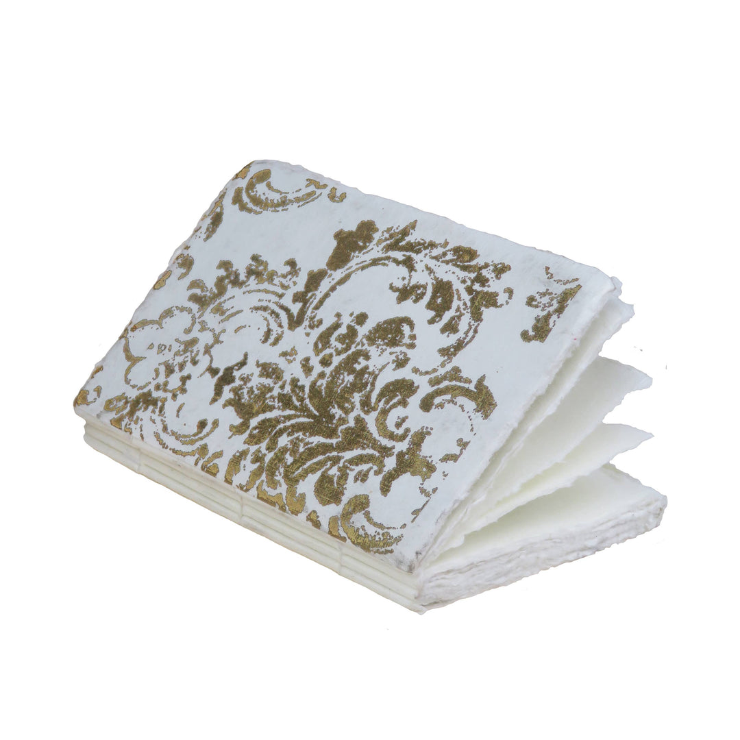 Grand Siècle -muistikirja sivulta kuvattuna: kultakuvioinen kansi ja käsintehdyt paperisivut. / Side view of a Grand Siècle notebook showing its gold-patterned cover and handmade paper pages.
