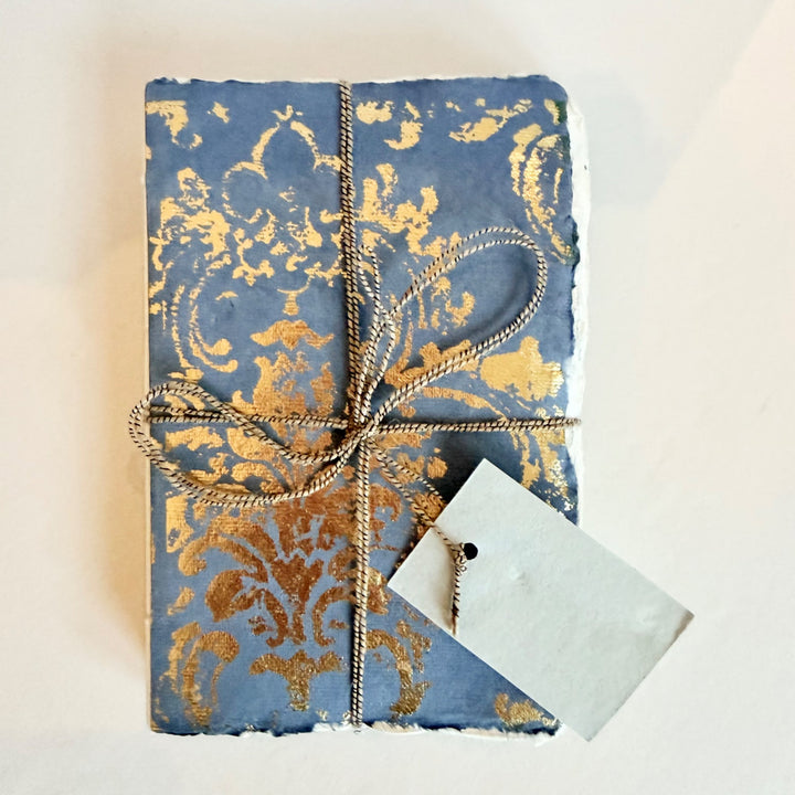 Grand Siècle -muistikirja, sininen kansi kullanvärisellä koristekuviolla ja nyöri. / Grand Siècle notebook with a blue cover, gold-coloured ornament and cord.