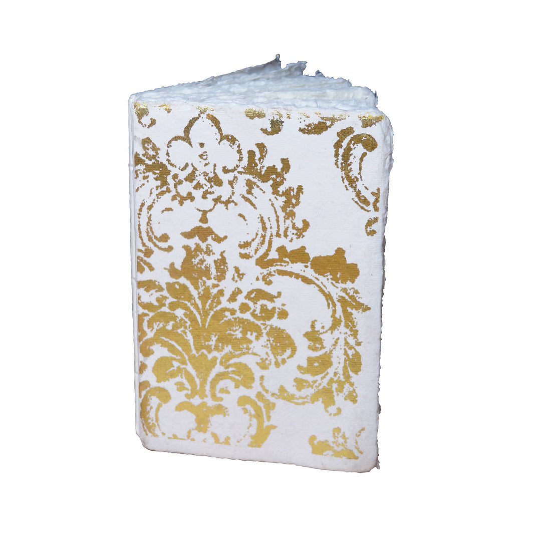 Valkoinen Grand Siècle -muistikirja, jonka kannessa on kullanvärinen koristekuvio. / White Grand Siècle notebook with a gold-coloured ornamental cover.