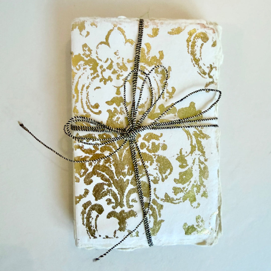 Grand Siècle -muistikirja, valkoinen kansi kullanvärisellä koristekuviolla ja nyöri. / Grand Siècle notebook with a white cover, gold-coloured ornament and cord.