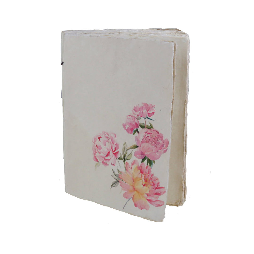 Vaalea muistikirja, jonka kannessa on vaaleanpunaisia pioneja. / Cream notebook with pink peonies on the cover.