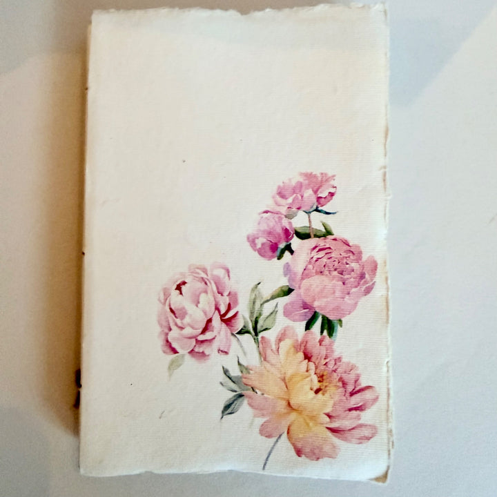 Vaalea käsintehty muistikirja, kuva-aiheena pionit. / Cream handmade notebook with pink peonies on the cover.