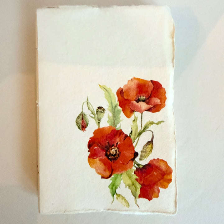 Vaalea käsintehty muistikirja, kuva-aiheena unikko. / Cream handmade notebook with red poppies on the cover.