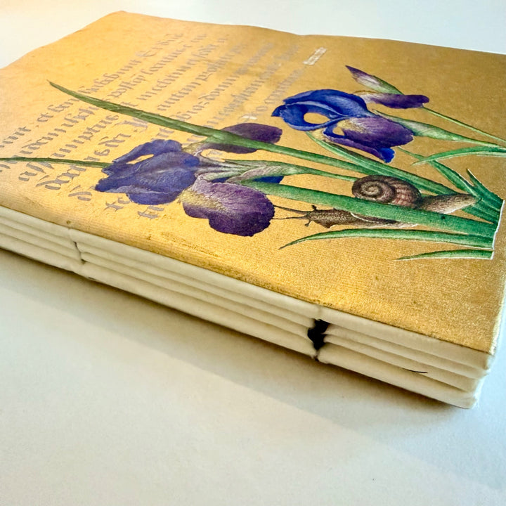 Iiris-muistikirjan kannen yksityiskohta, lankasidonta ja vaaleat paperisivut. / Detail of the iris notebook showing the cover, sewn binding and cream paper pages.