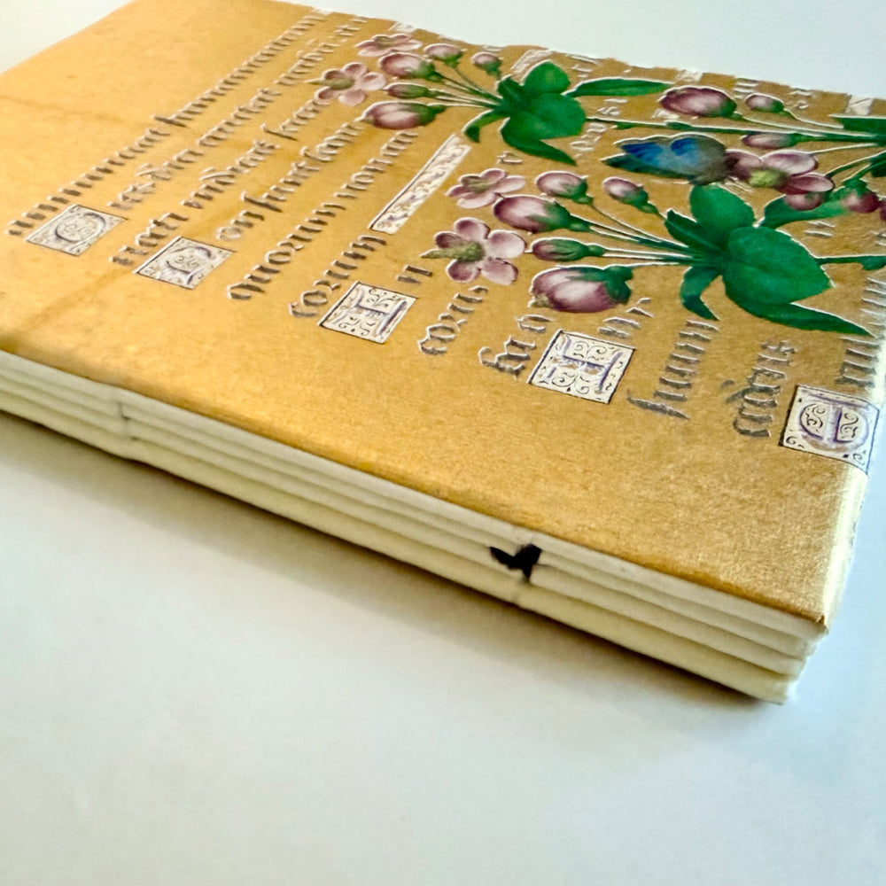 Kukka-aiheisen muistikirjan kääntöpuolen kuvitus, käsikirjoitusteksti ja lankasidonta. / Reverse cover of the floral notebook showing flowers, manuscript lettering and sewn binding.