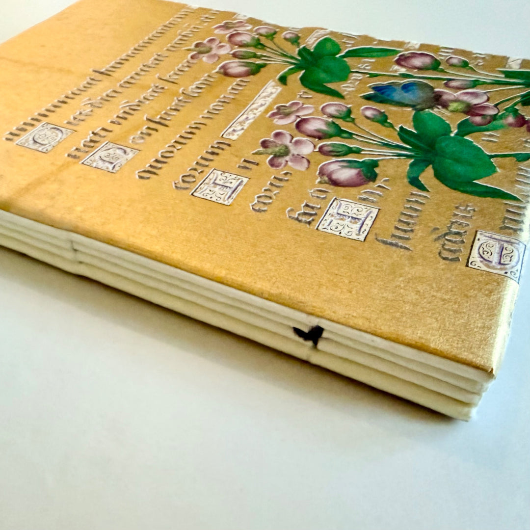Kukka-aiheisen muistikirjan kääntöpuolen kuvitus, käsikirjoitusteksti ja lankasidonta. / Reverse cover of the floral notebook showing flowers, manuscript lettering and sewn binding.