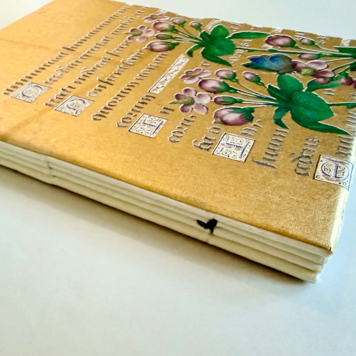 Kukka-aiheisen muistikirjan kääntöpuolen kuvitus, käsikirjoitusteksti ja lankasidonta. / Reverse cover of the floral notebook showing flowers, manuscript lettering and sewn binding.