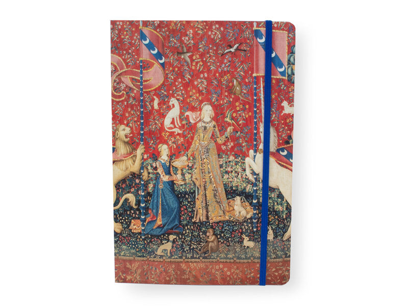 Nainen ja yksisarvinen -muistikirjan etukansi, punainen kuvakudosaihe, nainen, leijona, yksisarvinen ja sininen kuminauha. – Front cover of The Lady and the Unicorn notebook with a red tapestry design, a lady, lion, unicorn and blue elastic closure.