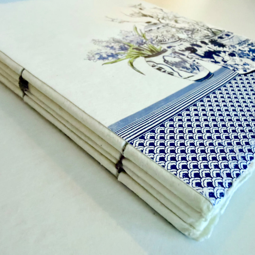 Maljakkoaiheisen muistikirjan lankasidonta ja sininen aaltokuvio kannen reunassa. / Detail of the vase notebook showing its sewn binding and blue wave border.