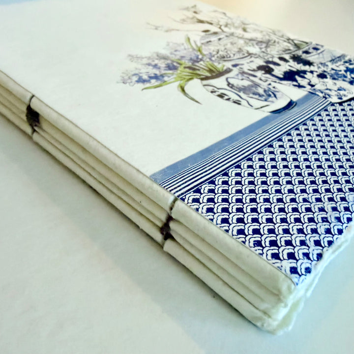 Maljakkoaiheisen muistikirjan lankasidonta ja sininen aaltokuvio kannen reunassa. / Detail of the vase notebook showing its sewn binding and blue wave border.