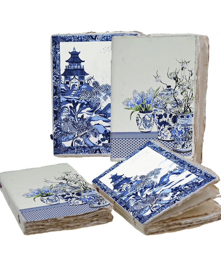 Sinivalkoiset muistikirjat, joiden kansissa on puutarhamaisema tai kukkia ja koristeellisia maljakoita. / Blue and white notebooks with garden scenery or flowers and decorative vases on the covers.