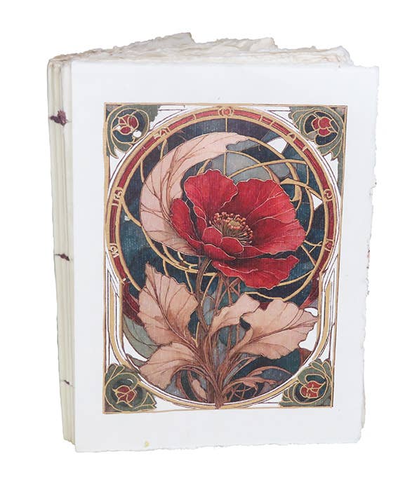 Vaalea muistikirja, jonka kannessa on punainen unikko tummanvihreässä art nouveau -koristekehyksessä kullanvärisin yksityiskohdin. / Cream notebook with a red poppy in a dark green Art Nouveau frame with gold-coloured details.