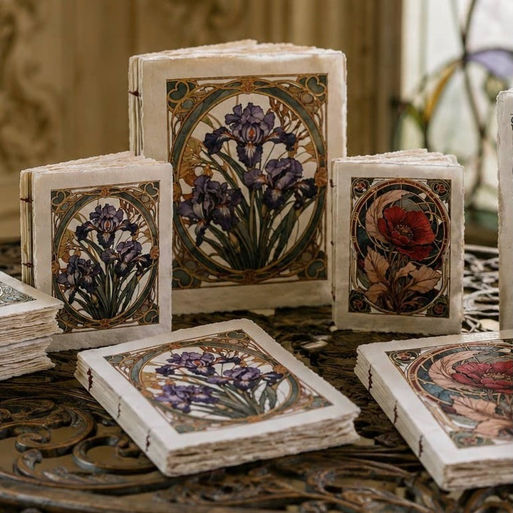 Art nouveau -muistikirjoja, joiden kansissa on violetteja iiriksiä ja punaisia unikoita koristeellisissa kehyksissä. / Art Nouveau notebooks with purple irises and red poppies in decorative frames.