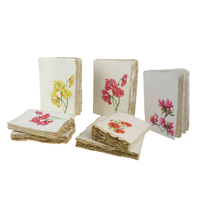Kukkakuvioisia muistikirjoja, joiden kansissa on punaisia ja keltaisia tulppaaneja, magnolioita ja unikoita. / Floral notebooks with red and yellow tulips, magnolias and poppies on the covers.