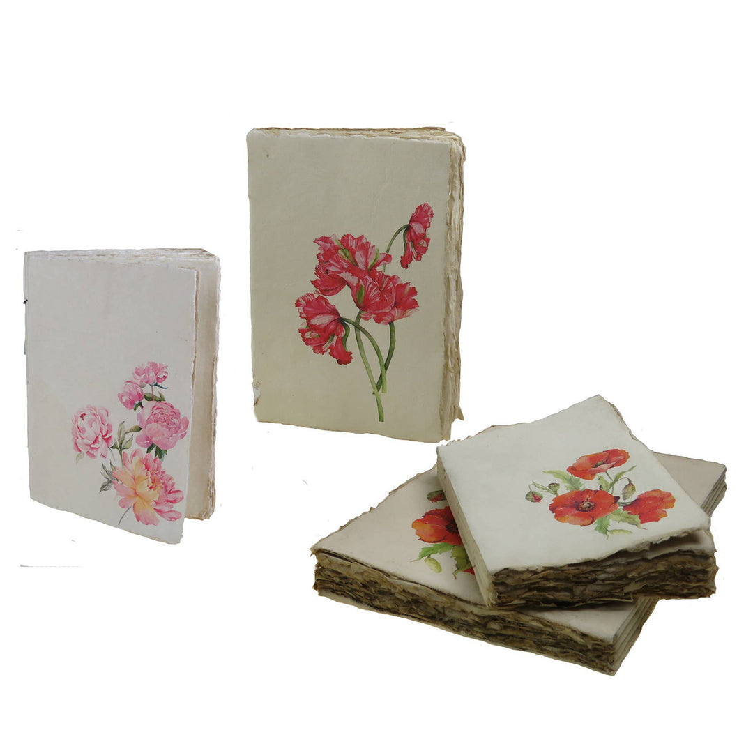Kolme kukkakuvioista muistikirjaa, joiden kansissa on vaaleanpunaisia pioneja, punaisia tulppaaneja ja unikoita. / Three floral notebooks with pink peonies, red tulips and poppies on their covers.
