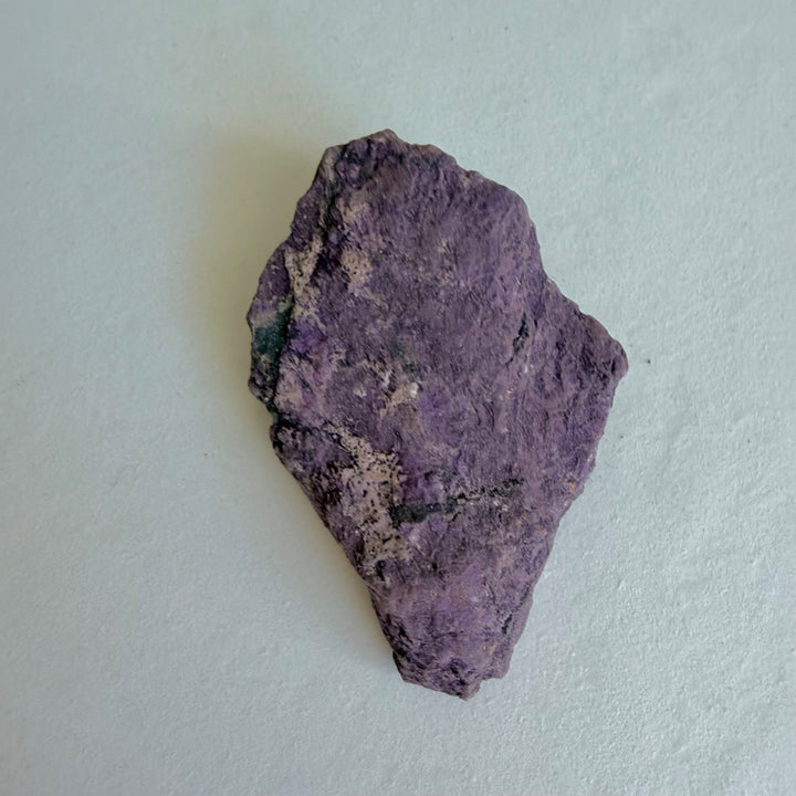Purpurite Stone 1 viewed from the side, a rough stone in purple and dark tones.