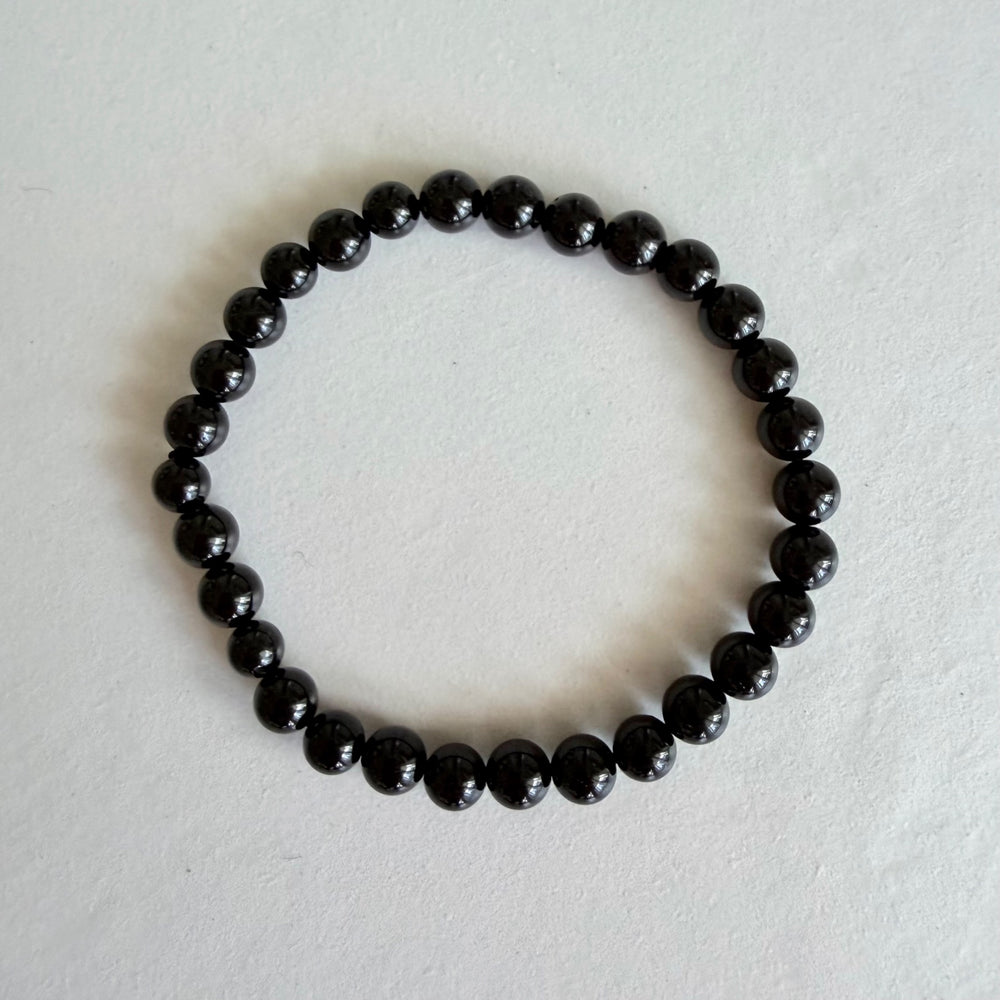 Bracelet made from polished black tourmaline beads, photographed from above on a pale background.