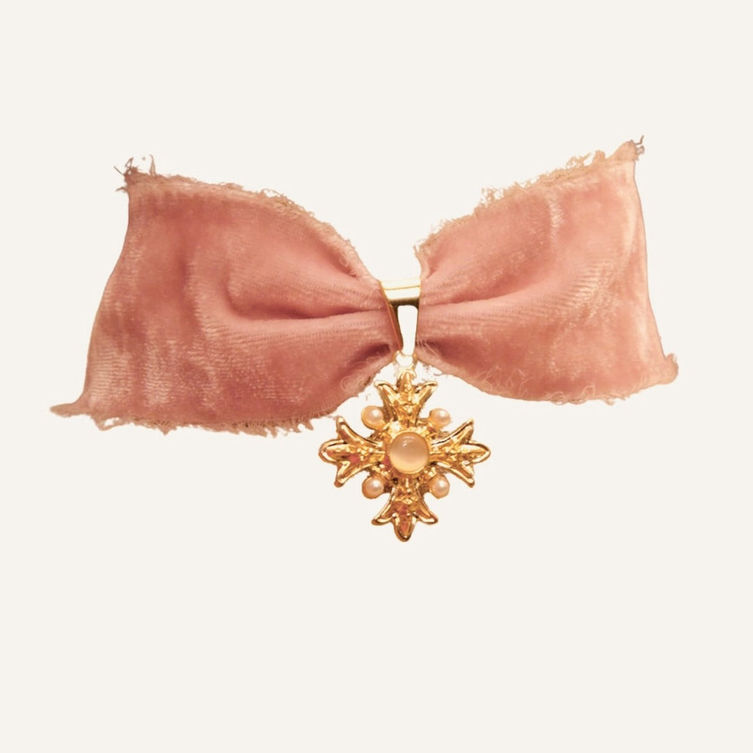 Vaaleanpunainen silkkisamettinen choker-kaulakoru, jossa on helmimäisin koristein somistettu kullanvärinen ristiriipus.